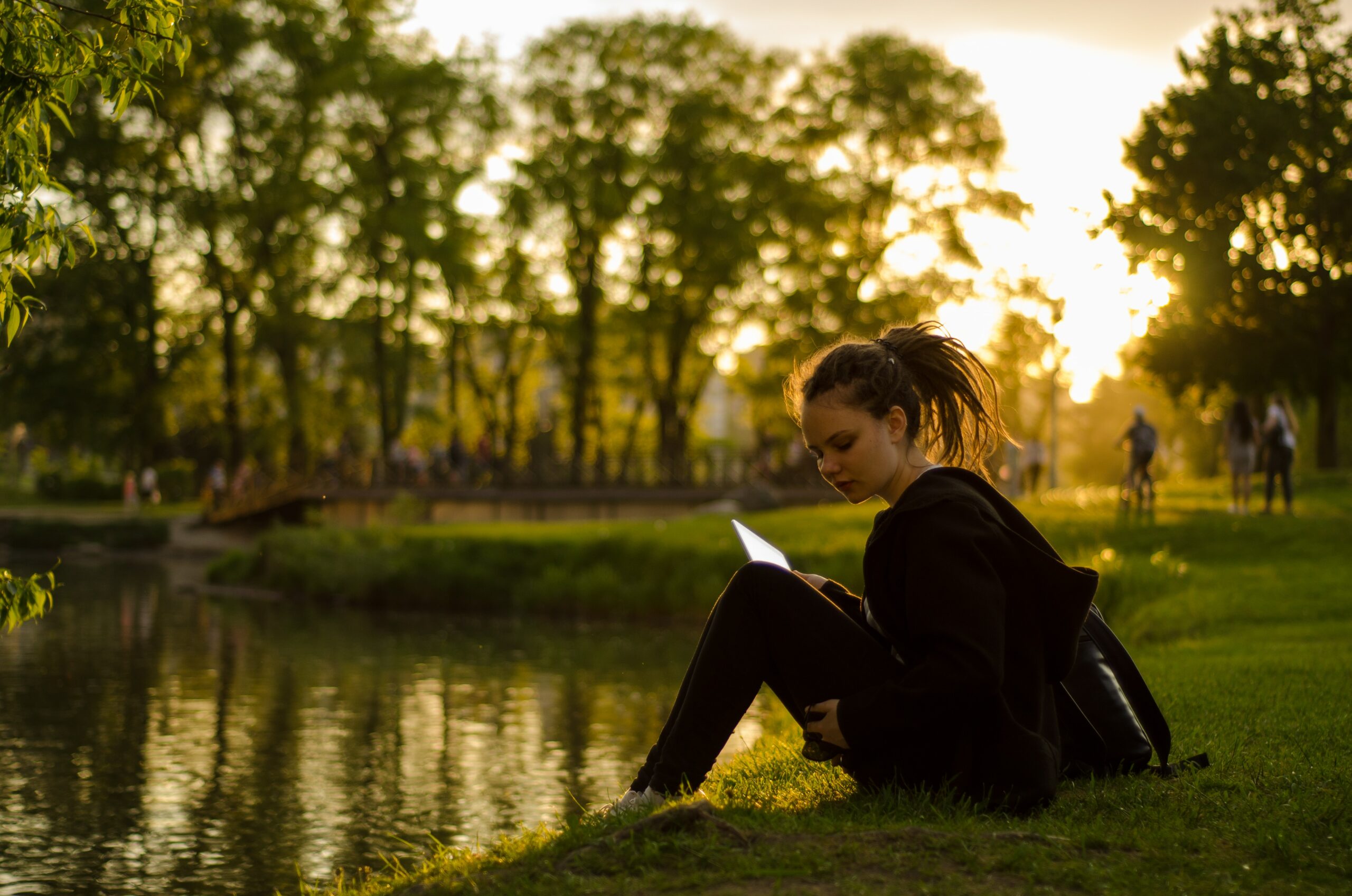 woman sitting on grass field beside body of water during golden hour