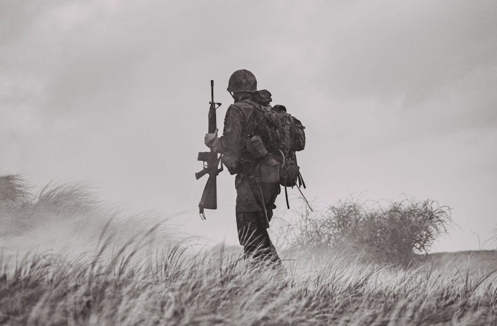 grayscale photo of man in black jacket and pants holding rifle