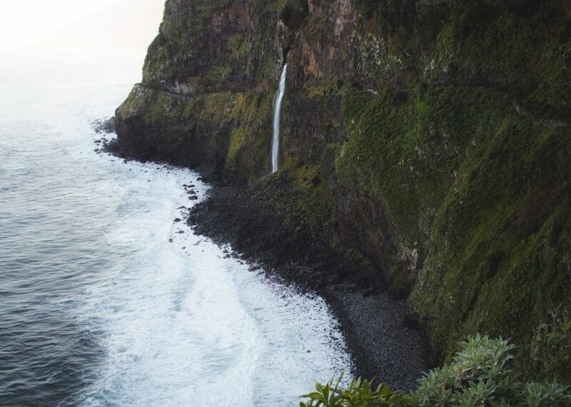 A waterfall on the side of a cliff next to the ocean