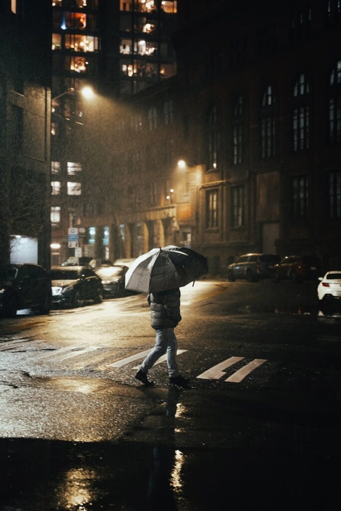 A person walks across a wet street in the rain.